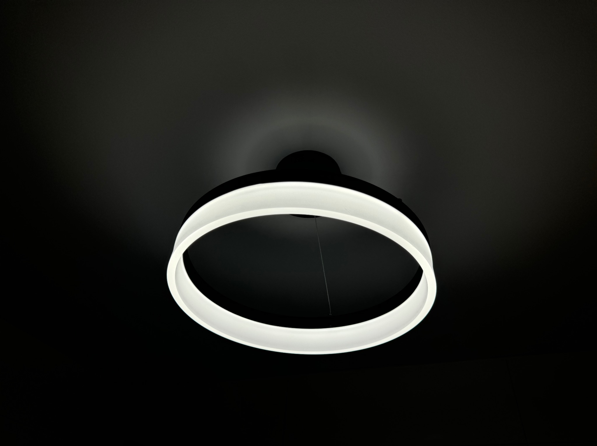 Nowoczesna okrągła lampa LED z białym światłem zawieszona na czarnym suficie, widok z dołu.