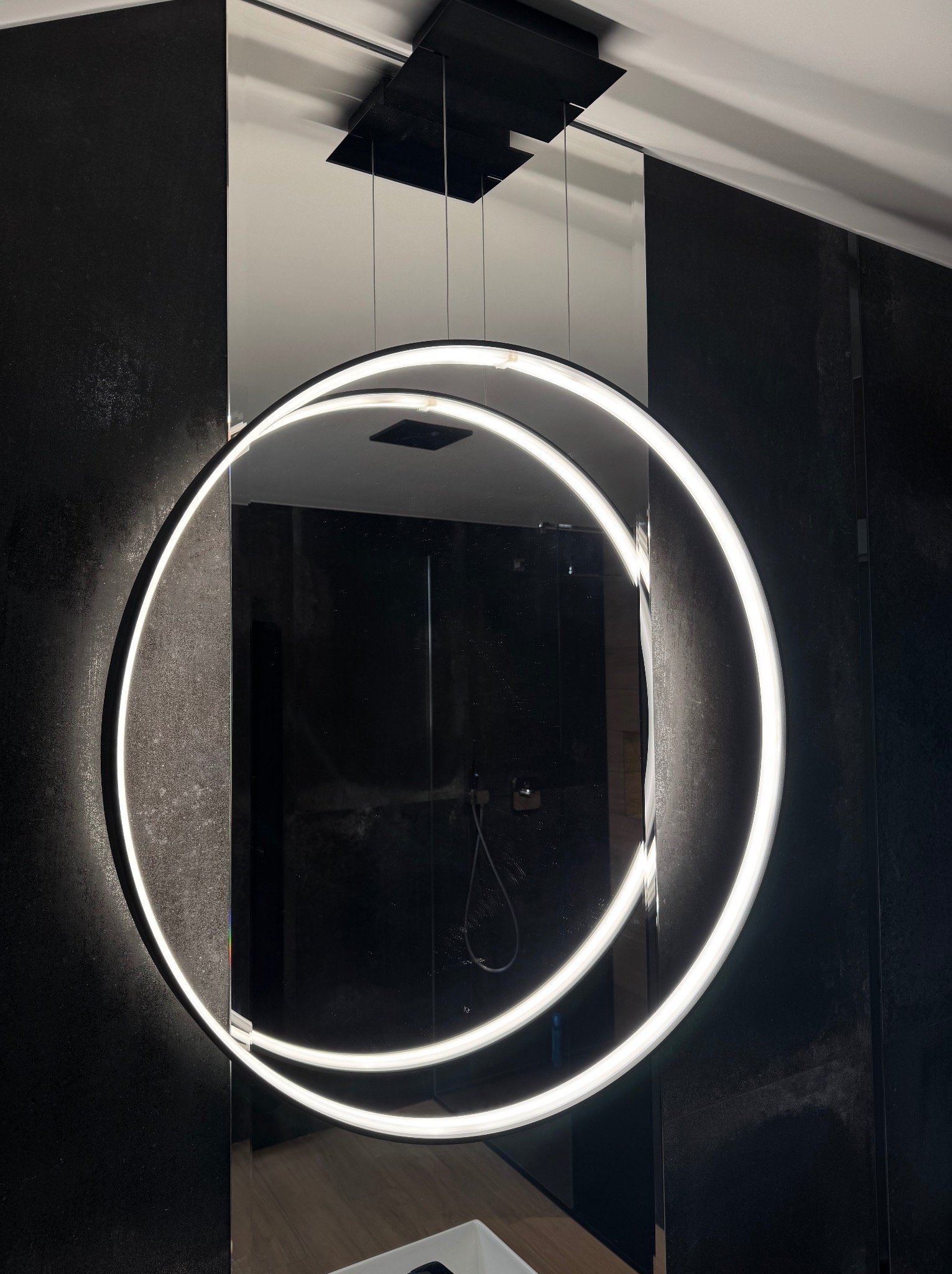 Nowoczesne oświetlenie łazienkowe: okrągłe lampy LED zawieszone nad lustrem, czarne płytki na ścianach, minimalistyczny design. Unikalny układ lamp.