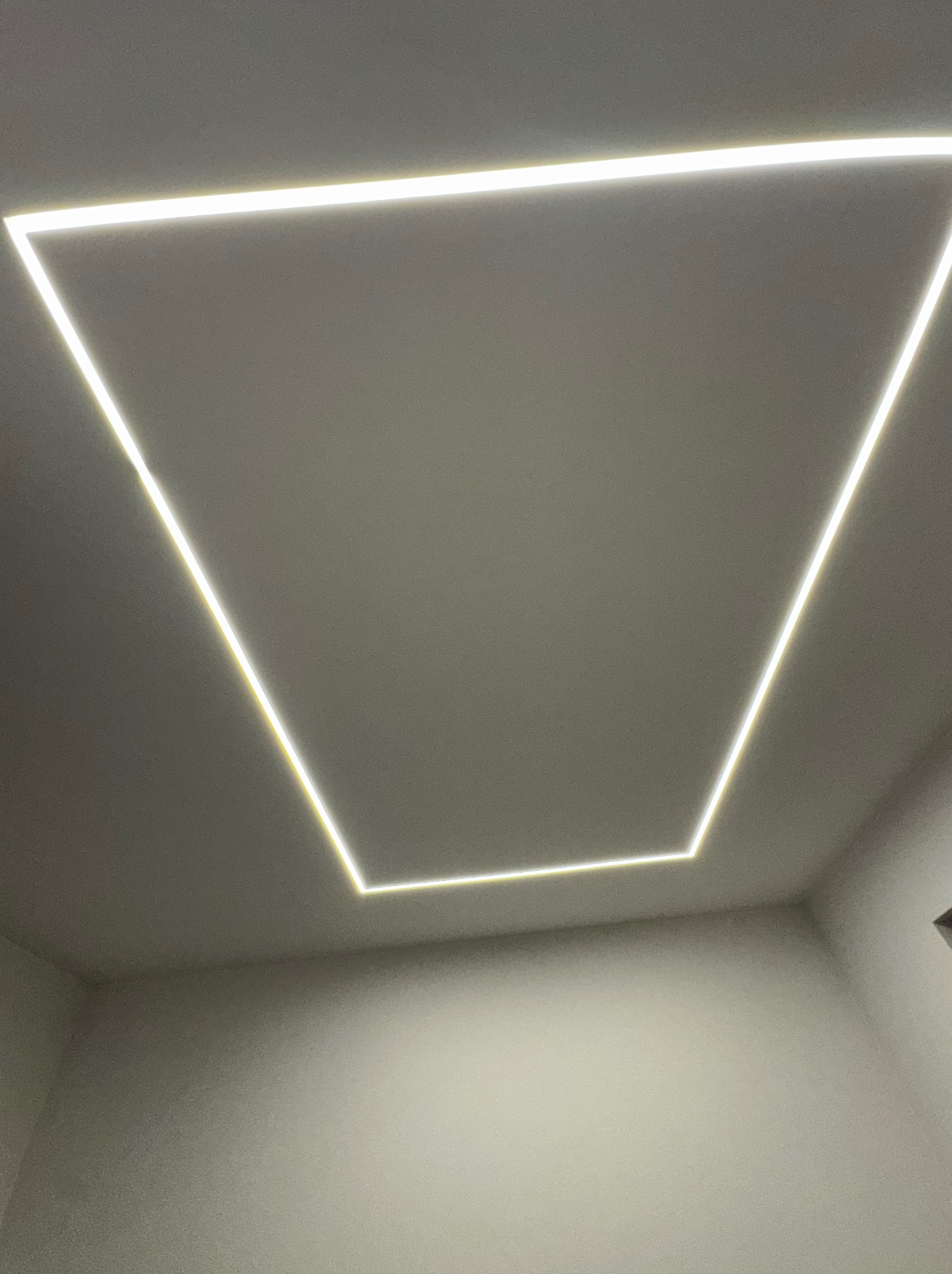 Nowoczesne oświetlenie sufitowe LED w kształcie trapezu, emitujące jasne, równomierne światło. Minimalistyczny design w neutralnej kolorystyce.