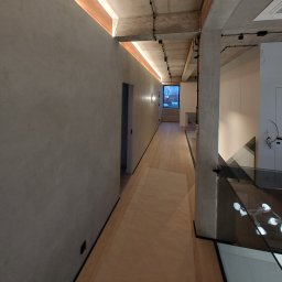 PROFITECH - Borys Tustanovskyi - Nowoczesny korytarz z gładkimi, szarymi ścianami, drewnianą podłogą i podświetlanym sufitem, widok na okno na końcu korytarza.