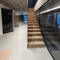 PROFITECH - Borys Tustanovskyi - Nowoczesne schody drewniane z szklaną balustradą w minimalistycznym wnętrzu z betonowym sufitem i białymi ścianami, widoczne przez szklane ściany rusztowanie.
