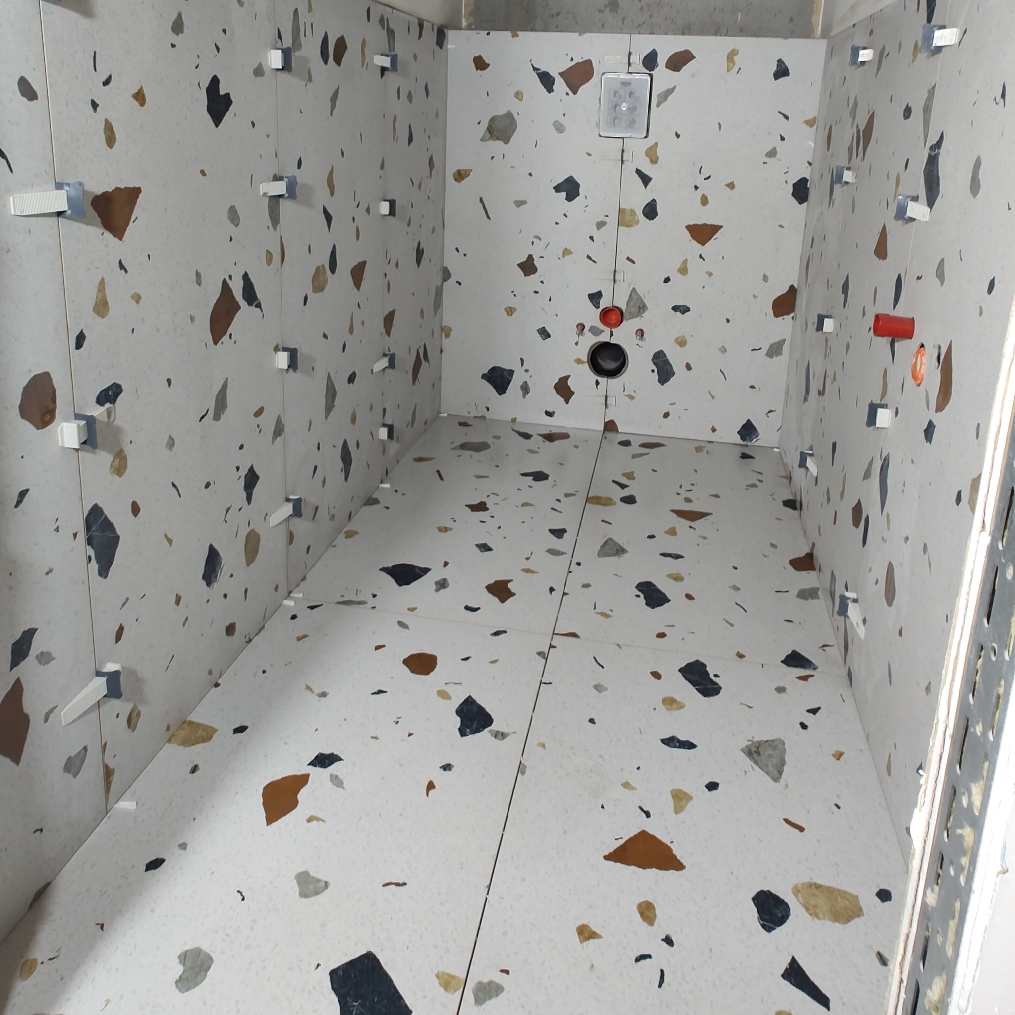 Układanie płytek podłogowych i ściennych z wzorem lastryko w trakcie remontu łazienki, widoczne plastikowe krzyżyki dystansowe i otwory na instalacje.