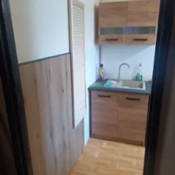 Funkcjonalna kuchnia po remoncie w Tychach. Drewniane szafki, jasne ściany i podłoga. Widoczne detale wykończenia, takie jak armatura i akcesoria.