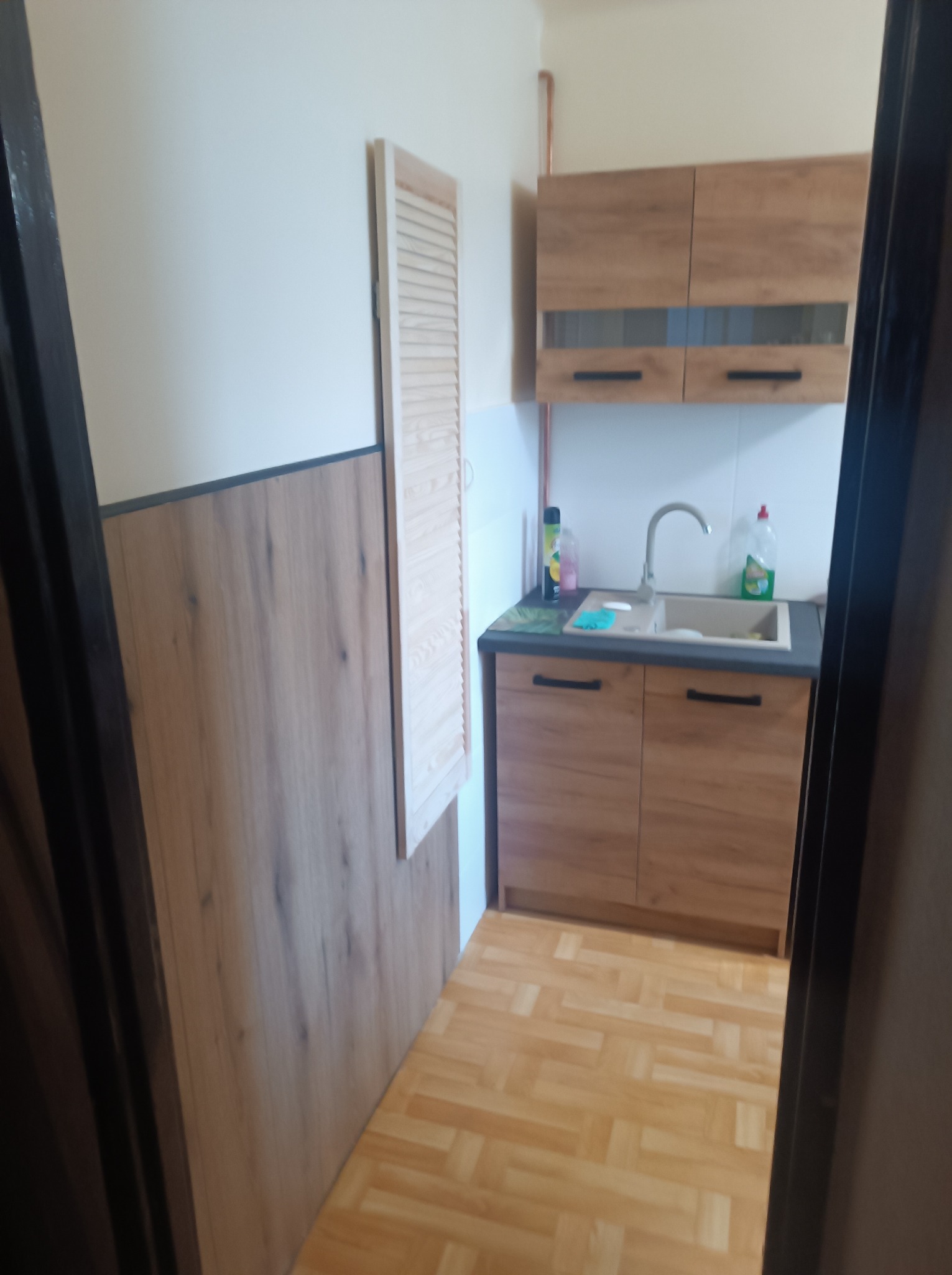 Funkcjonalna kuchnia po remoncie w Tychach. Drewniane szafki, jasne ściany i podłoga. Widoczne detale wykończenia, takie jak armatura i akcesoria.