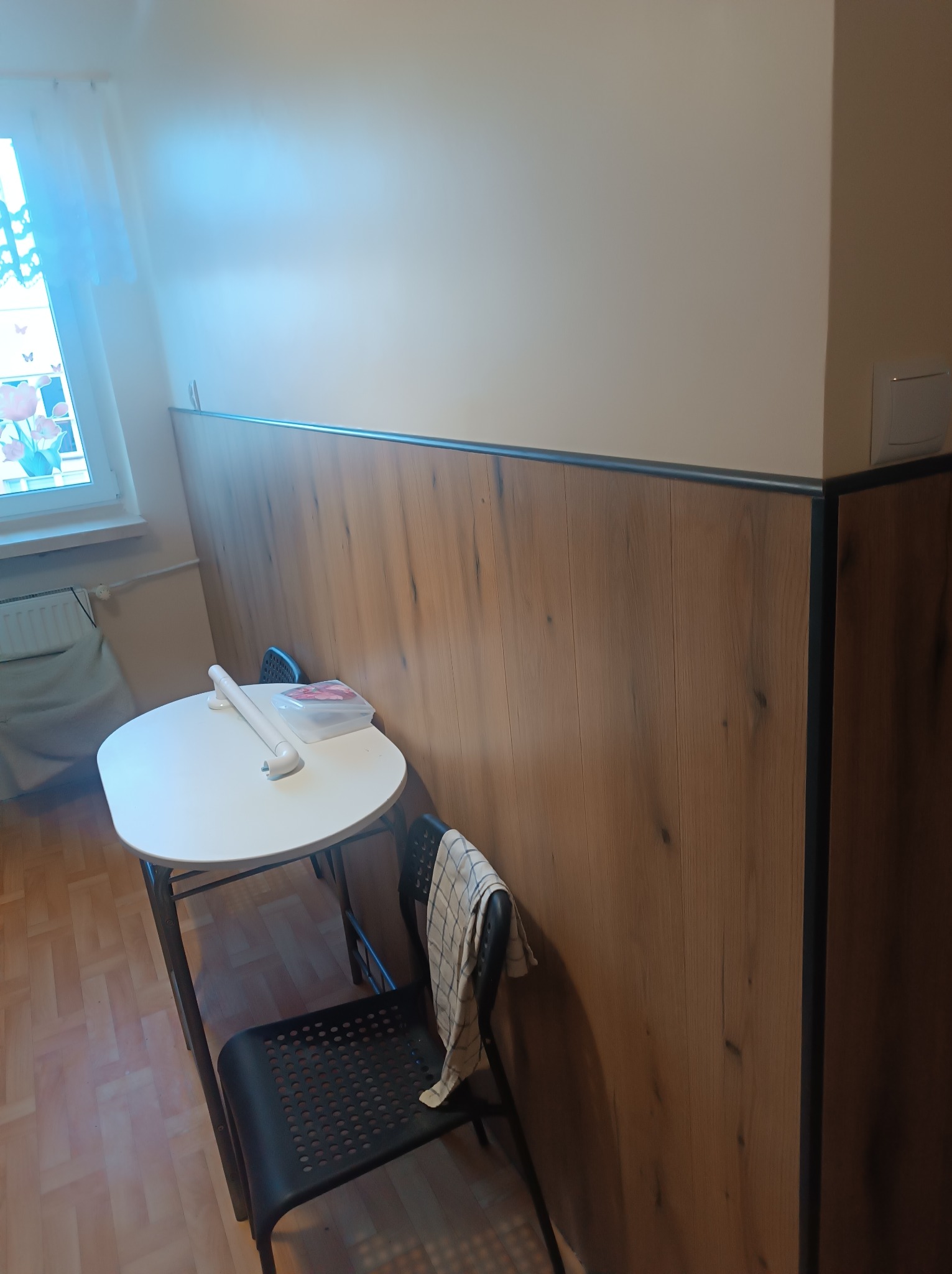 Ściana z drewnianą okładziną, stół z akcesoriami i krzesło. Okładzina przypomina panele ścienne, wykończona czarną listwą. Widok na fragment odnowionego wnętrza.