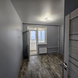 Natalia Meliakh Meliastrong - Szare wnętrze pokoju po remoncie z drzwiami z efektem drewna, marmurową podłogą, białym grzejnikiem i nowoczesną lampą sufitową.