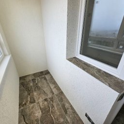 Natalia Meliakh Meliastrong - Wnętrze balkonu z szarobrązową marmurkową podłogą, białe ściany z fakturą baranka i białe okno z marmurowym parapetem.