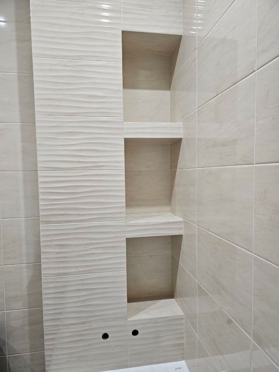 Wykończona wnęka z półkami w łazience, obłożona płytkami w odcieniach beżu, z widocznymi otworami na baterię, prezentująca nowoczesny design.