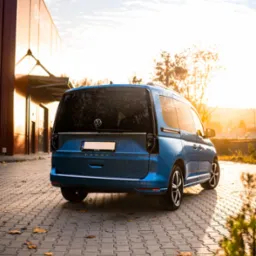 Błękitny Volkswagen Caddy zaparkowany na brukowanym placu, jesienne liście, zachodzące słońce odbija się w szybach