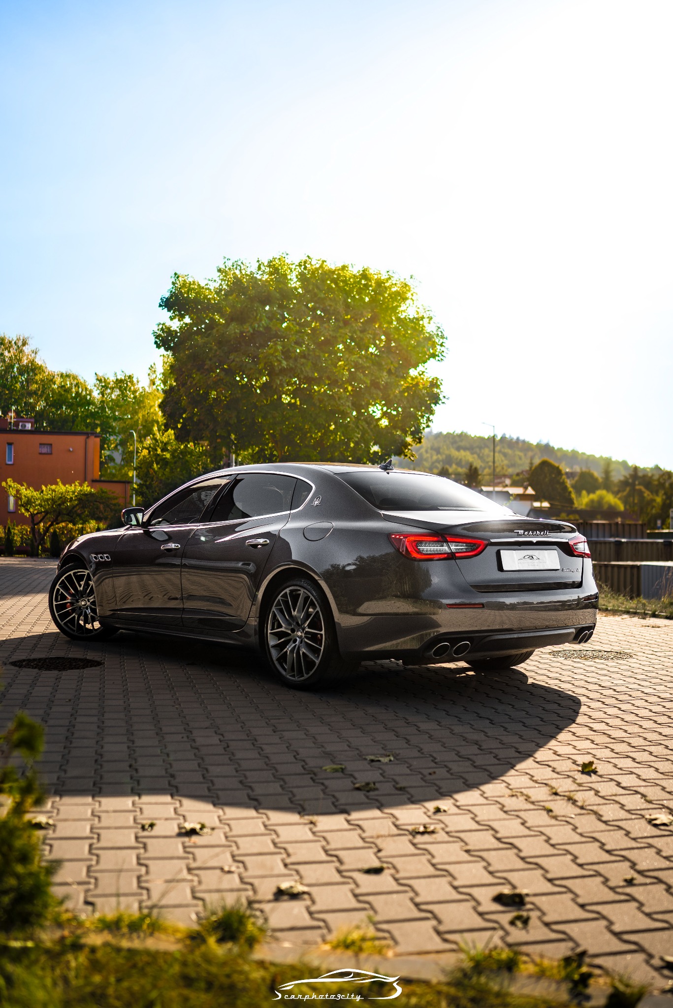 Szary samochód Maserati Quattroporte sfotografowany z tyłu, zaparkowany na brukowanej powierzchni w słoneczny dzień.