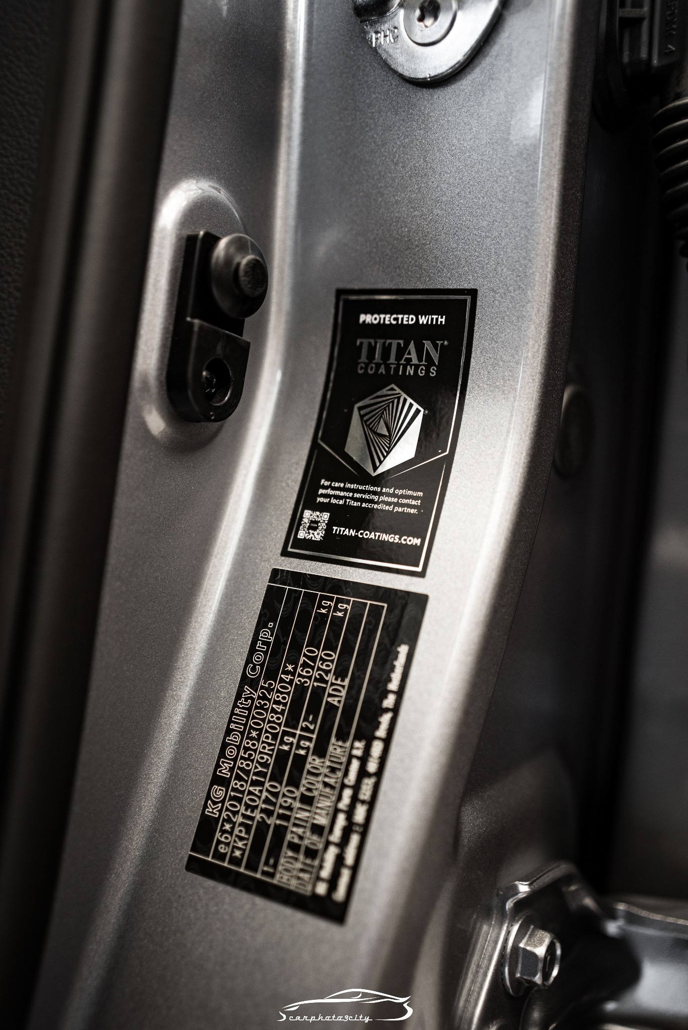 Szczegółowe ujęcie srebrnego lakieru na drzwiach samochodu z naklejką informacyjną Titan Coatings, podkreślającą ochronę powłoki.