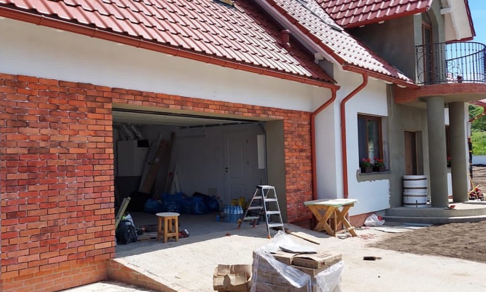 Wykończenie elewacji budynku z garażem cegłą klinkierową, widoczne rusztowanie, narzędzia i materiały budowlane.