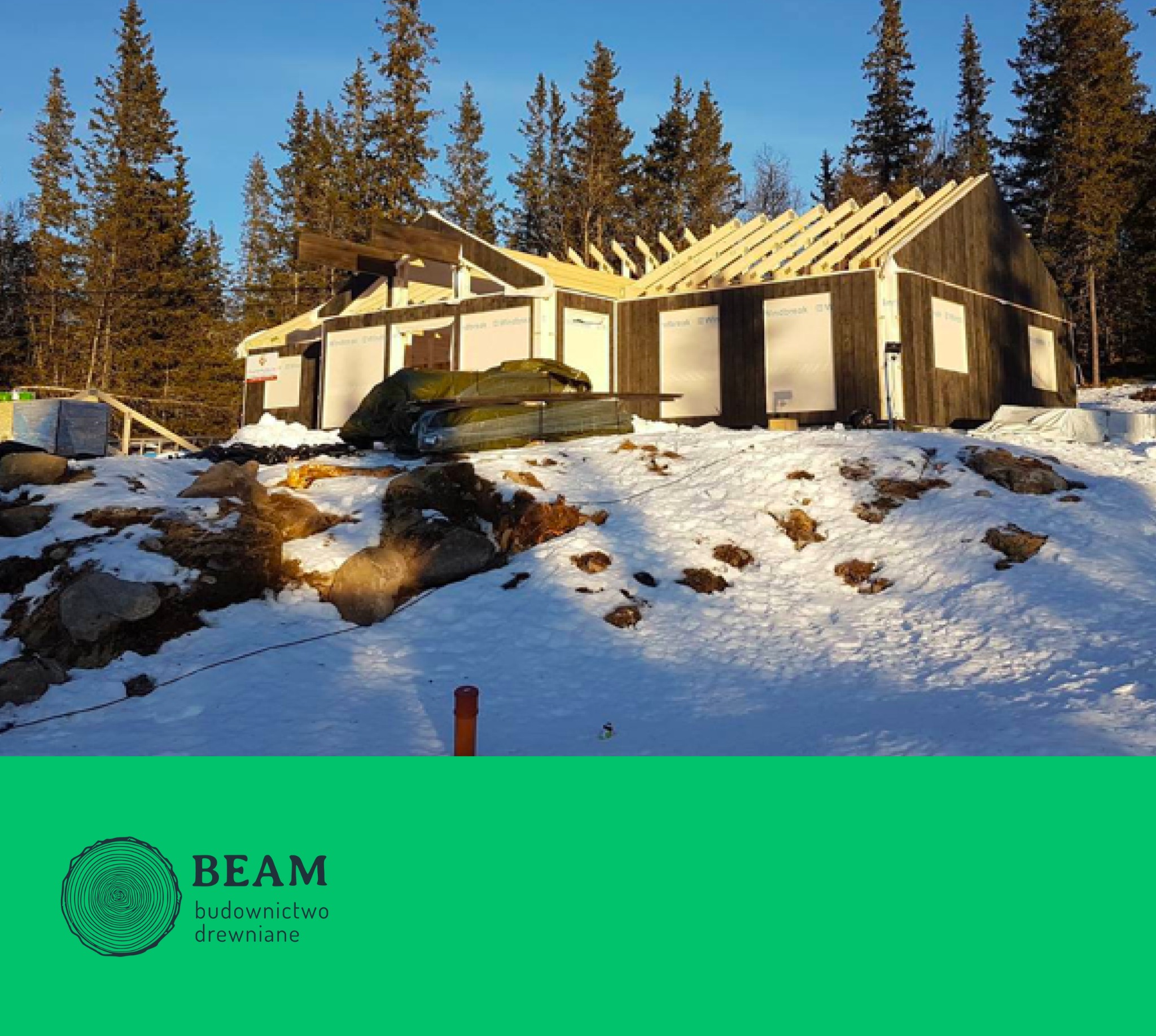 Wznoszony dom szkieletowy na ośnieżonej działce, widoczne drewniane elementy konstrukcyjne oraz folia wiatroizolacyjna, w tle las iglasty i błękitne niebo.