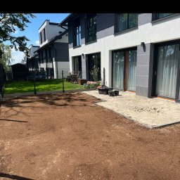 Aftergarden- Ogrody Premium - Przygotowany teren pod trawnik z wyrównaną ziemią i obrzeżami, przylegający do tarasu z piaskiem, nowoczesny dom w tle.