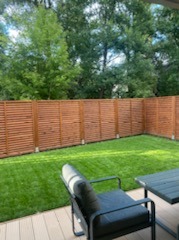 Kraków: Nowoczesny ogród z równo przystrzyżonym trawnikiem i drewnianym ażurowym ogrodzeniem. Na pierwszym planie fragment tarasu z meblami ogrodowymi.