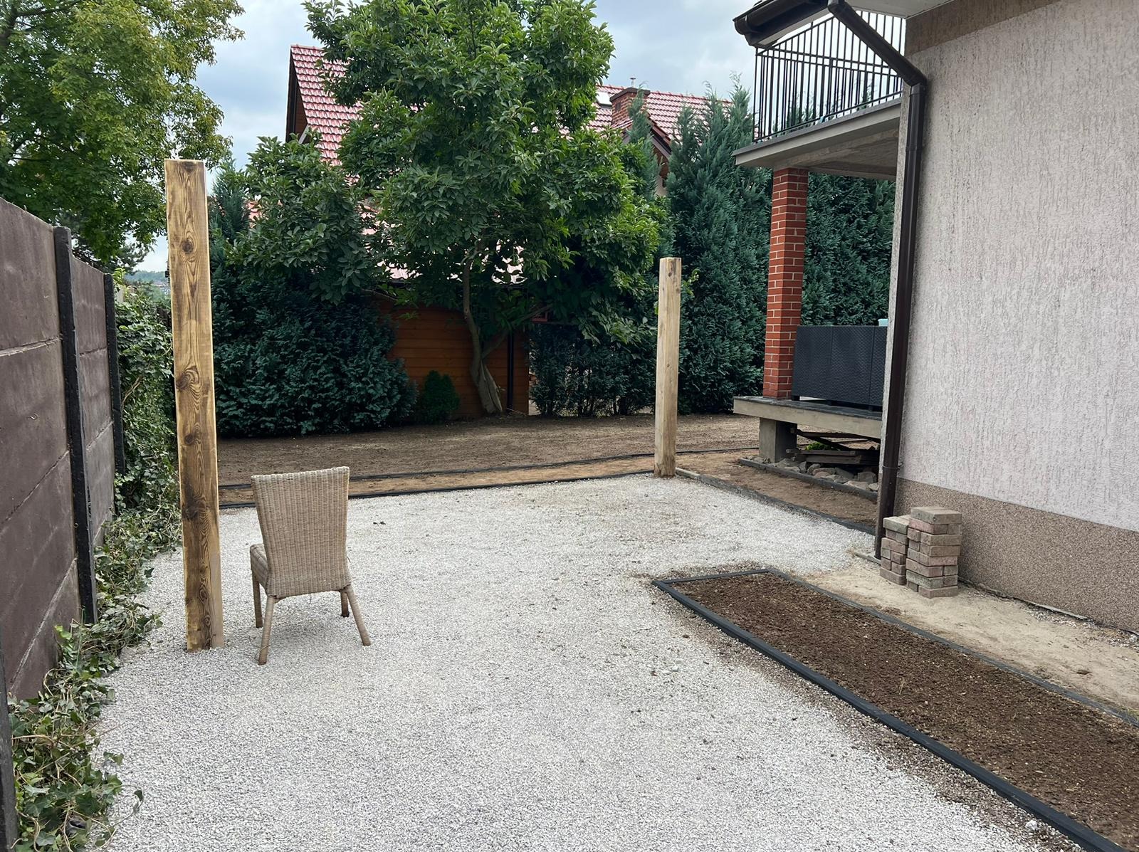 Przygotowany teren pod ogród z wysypanym białym żwirem, widoczne drewniane słupki, obrzeża rabat i krzesło wiklinowe