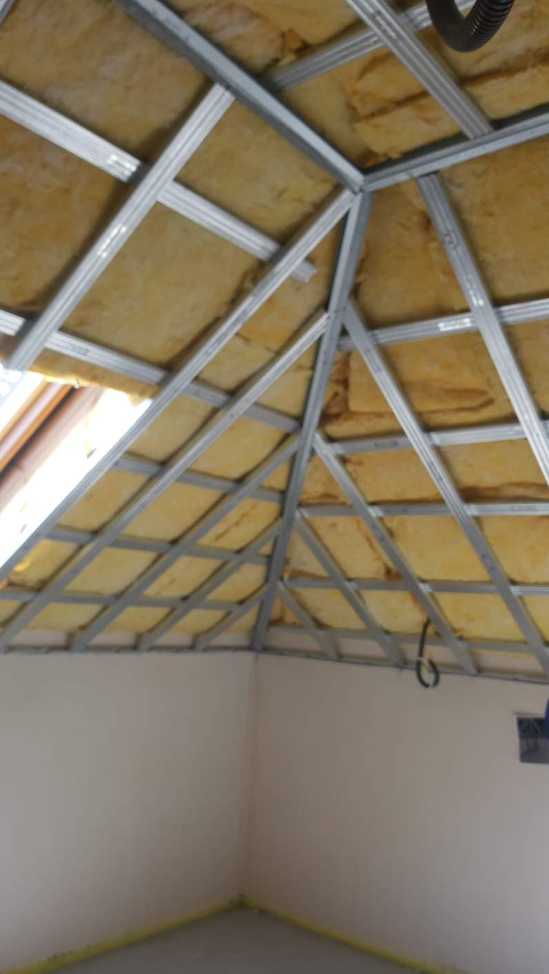 Skośny sufit poddasza z widoczną izolacją z wełny mineralnej i metalową konstrukcją szkieletową przygotowaną pod montaż płyt gipsowo-kartonowych, widok od dołu.
