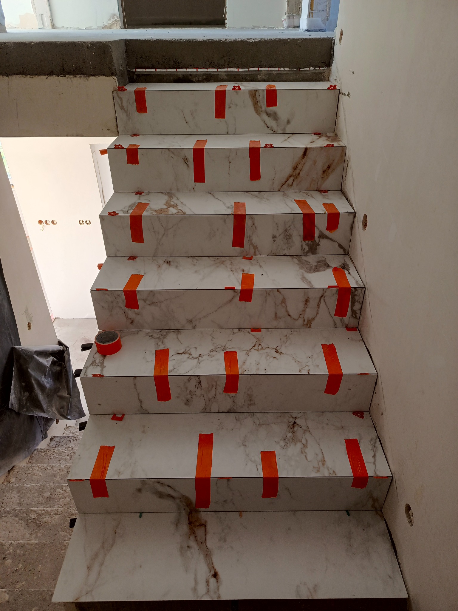 Wykończone marmurowe schody z pomarańczową taśmą zabezpieczającą w Teresinie. Widok z góry ukazuje detale płytek i etap prac wykończeniowych.