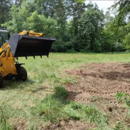 Żółta ładowarka przegubowa GG010 w Kędzierzynie-Koźlu na polu z częściowo zniwelowanym terenem, w tle drzewa.