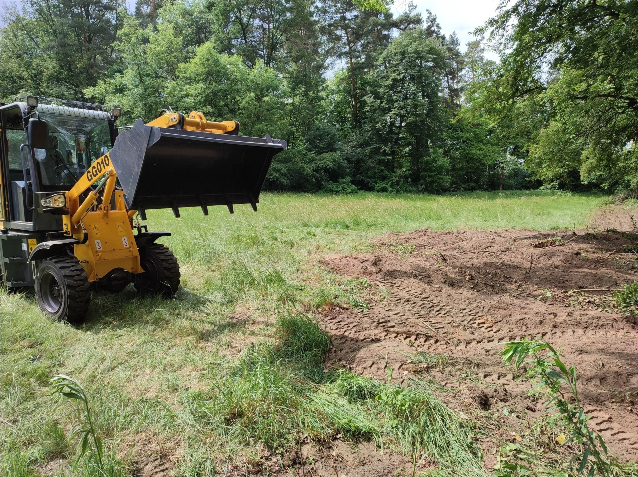 Żółta ładowarka przegubowa GG010 w Kędzierzynie-Koźlu na polu z częściowo zniwelowanym terenem, w tle drzewa.
