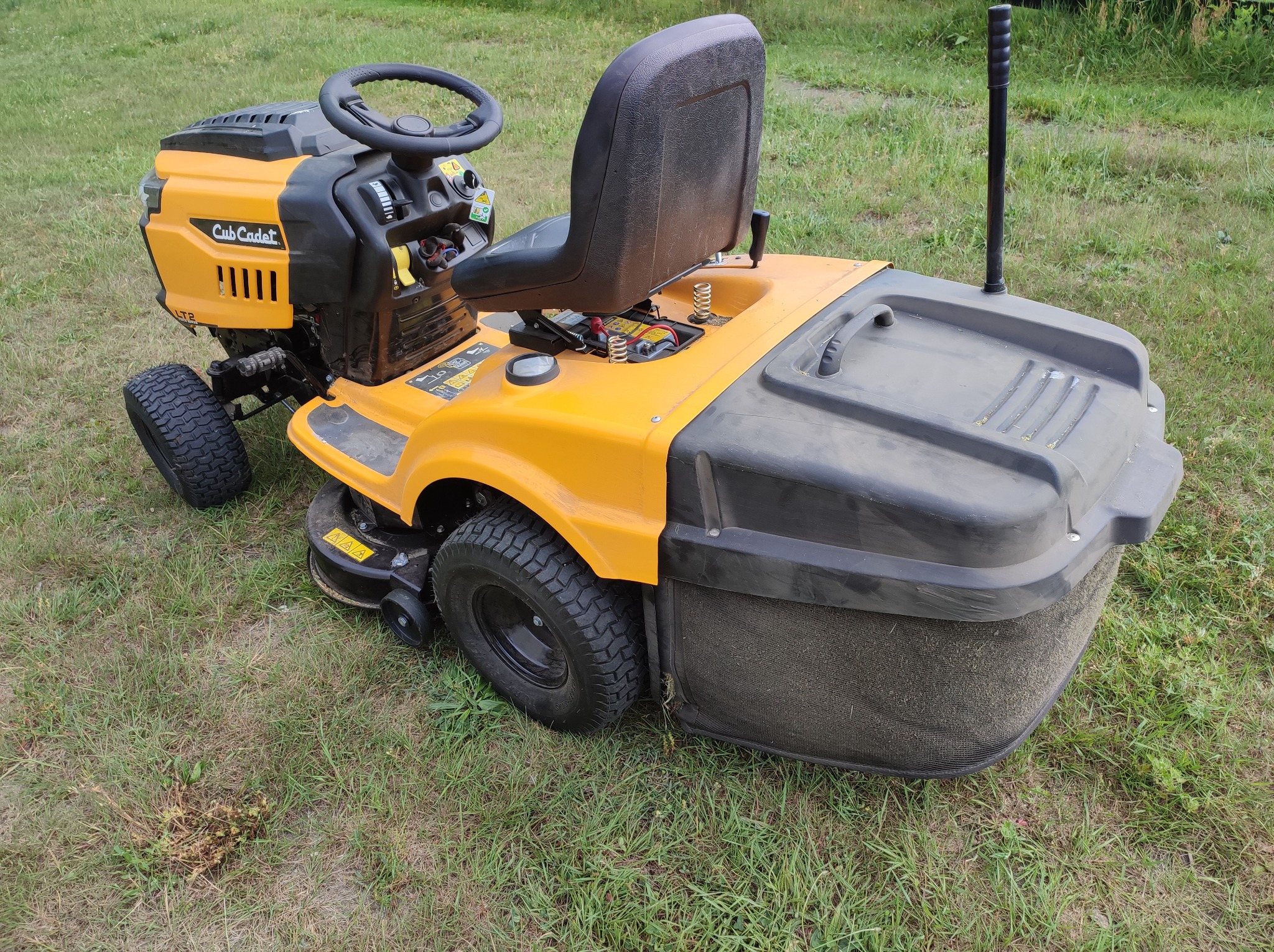 Żółto-czarna kosiarka traktorowa Cub Cadet z koszem na trawę, stojąca na trawniku.