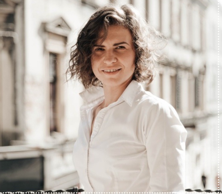 Portret uśmiechniętej kobiety w białej koszuli na tle jasnej architektury z balkonem, z lekkim efektem vintage.