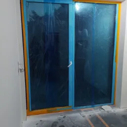 Okna zabezpieczone folią i taśmą malarską przed pracami wykończeniowymi. Widoczne ślady pyłu na podłodze. Przygotowanie do prac remontowych.