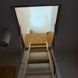 FAST-BUD Ireneusz Habura - Otwór strychowy z drewnianą składaną drabinką, widok z dołu. Widoczne płyty OSB i sprężyny mechanizmu. Ujęcie z perspektywy żabiej.