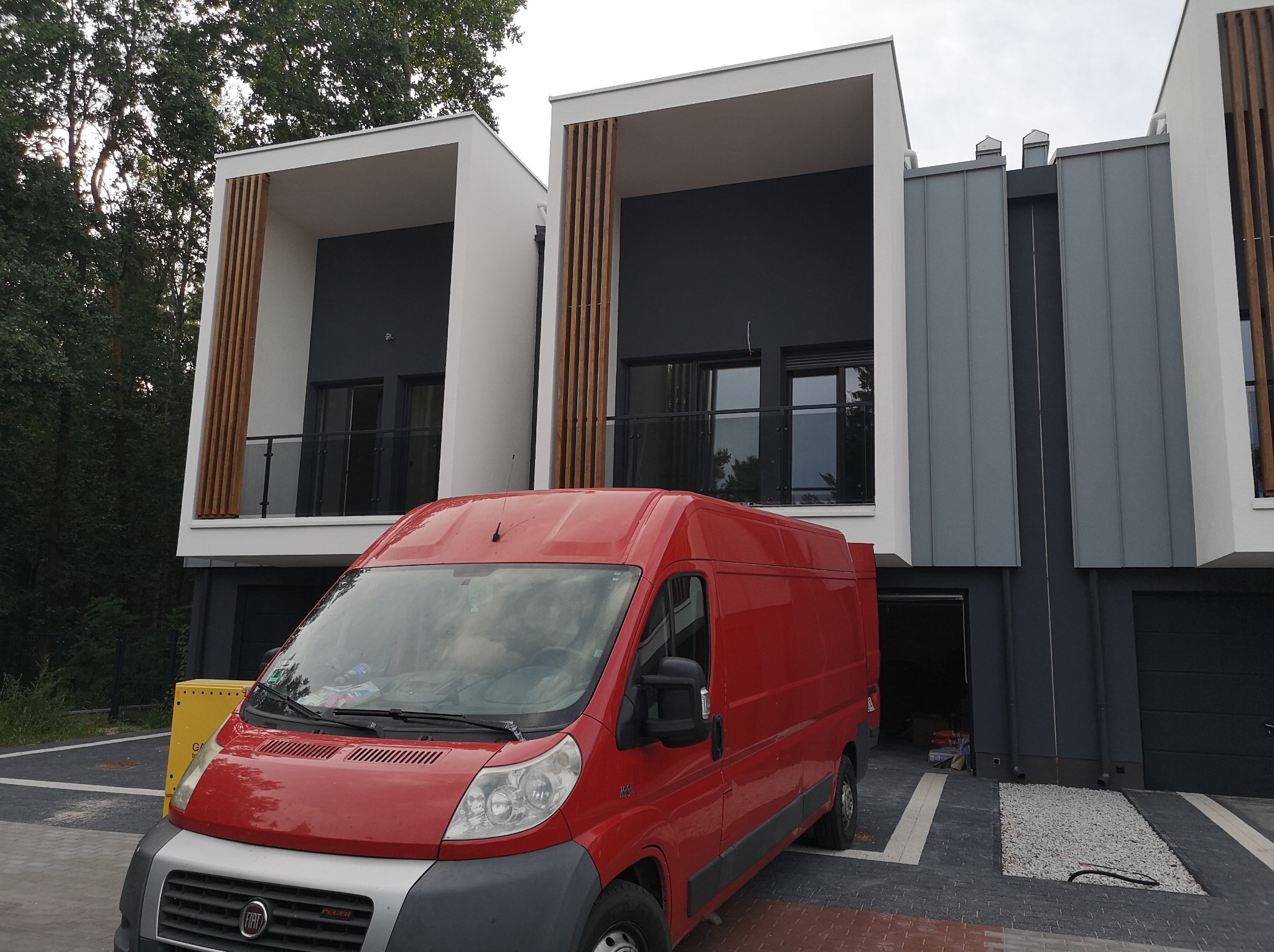 Nowoczesne budynki po malowaniu elewacji w Lubięcinie, z czerwonym samochodem dostawczym na pierwszym planie. Widoczne szare i białe elementy fasady.