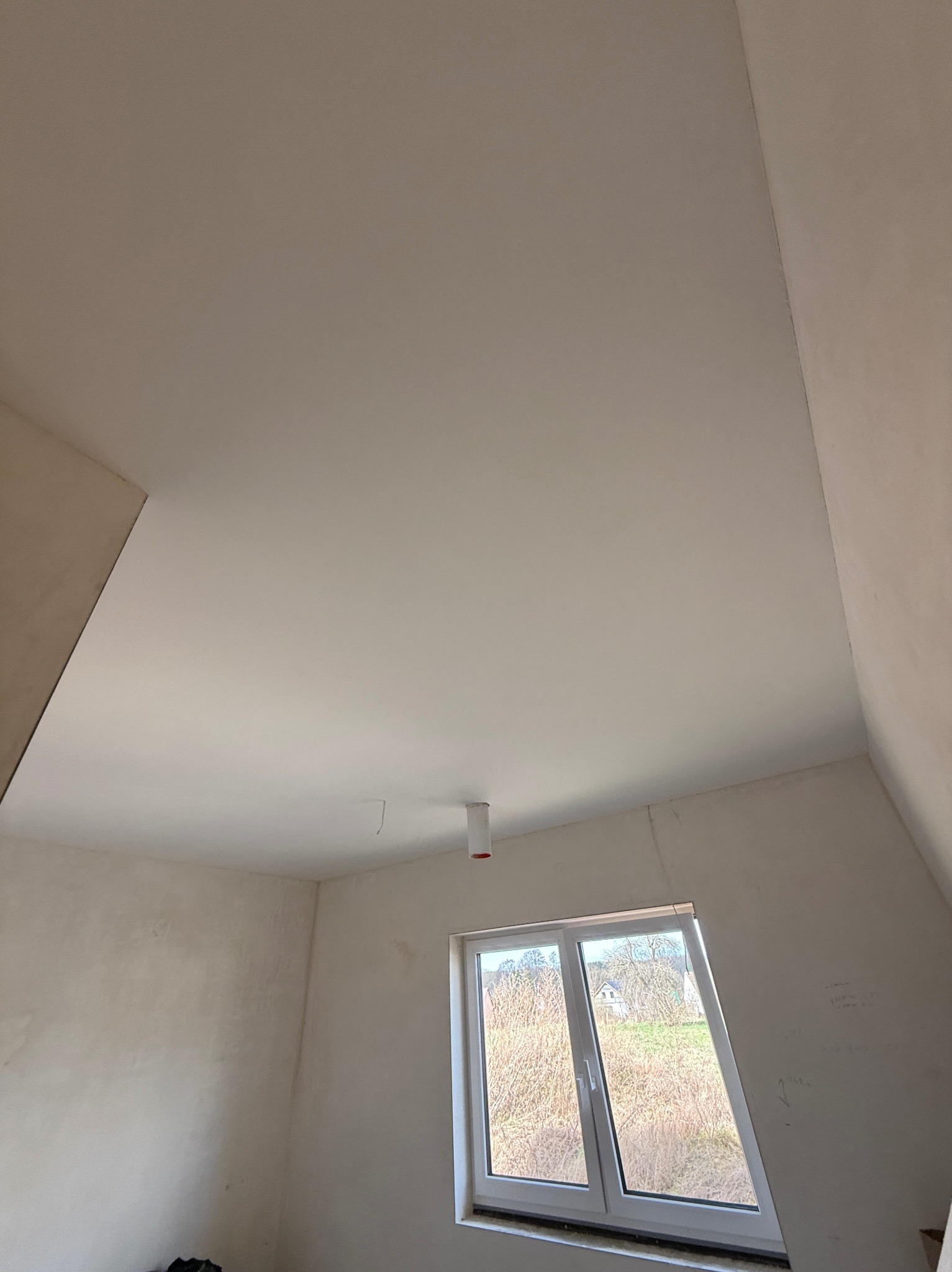 Wnętrze poddasza po szpachlowaniu, widoczne gładkie ściany i sufit, okno z widokiem na zewnątrz. Świeżo wykończone powierzchnie gotowe do dalszych prac.