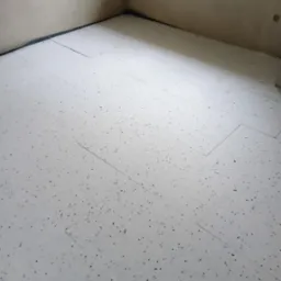 Białe płyty izolacyjne z czarnymi plamkami ułożone na podłodze w rogu pomieszczenia, widoczne ślady po gniazdkach elektrycznych na ścianie.