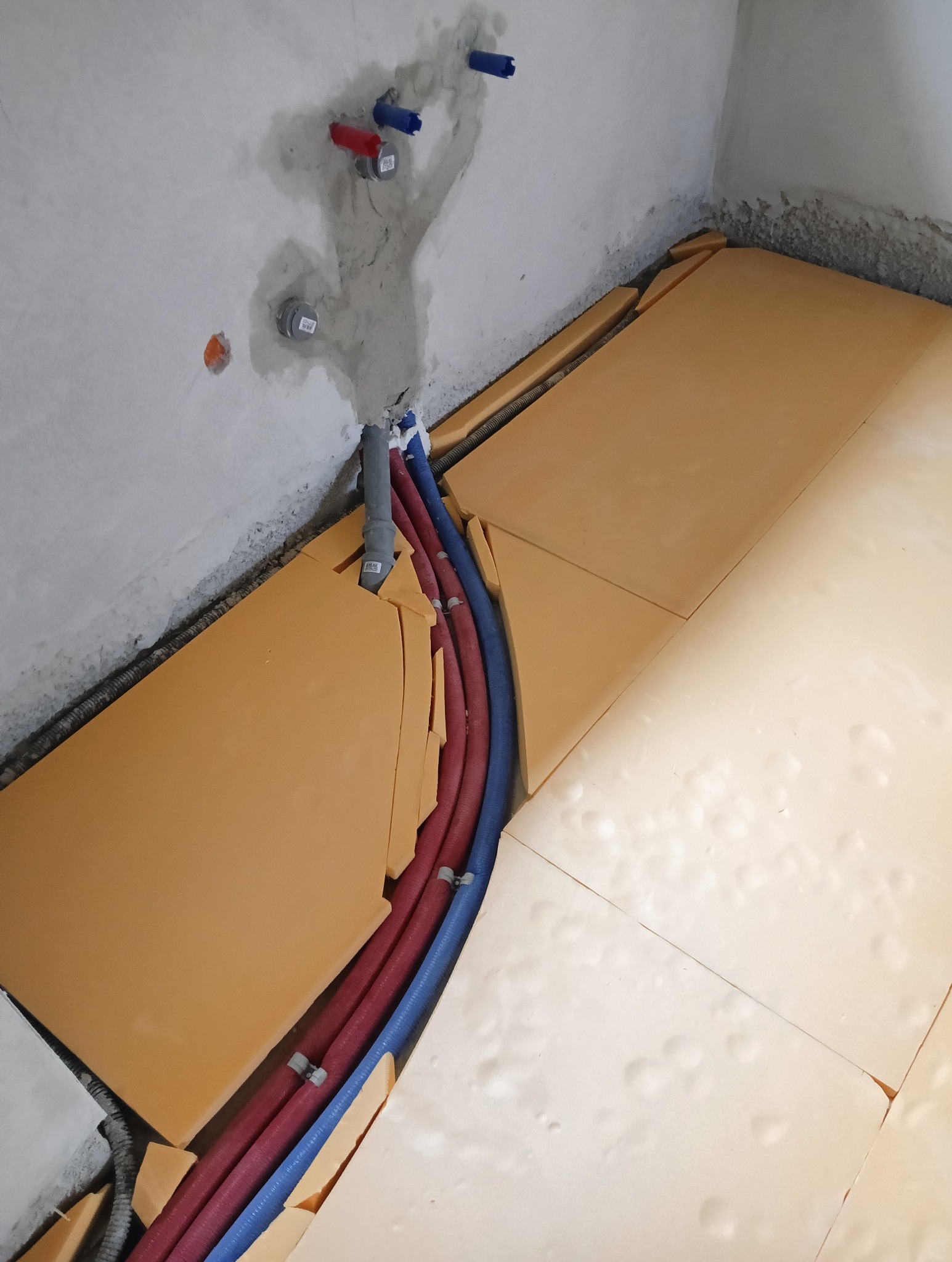 Przygotowanie do wylewki: rury ogrzewania podłogowego w izolacji z płyt styropianowych, widoczne przyłącza wodne w ścianie.