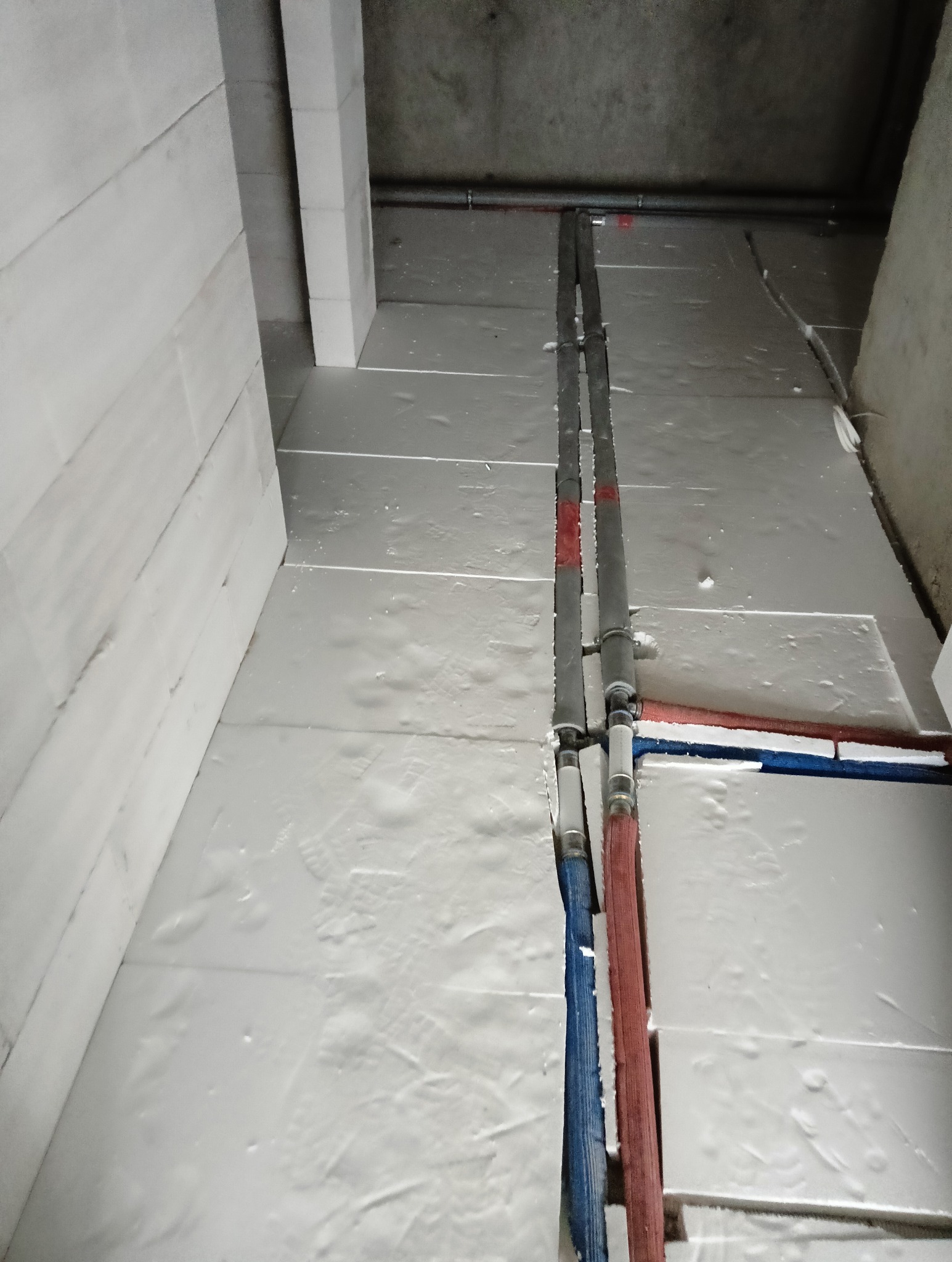 Izolacja fundamentów z białego styropianu, widoczne rury instalacyjne w kolorze niebieskim i czerwonym, surowy betonowy strop.
