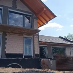 Dom w stanie surowym w Opalenicy z zamontowanymi oknami z roletami zewnętrznymi, widoczne przygotowania do dalszych prac wykończeniowych.