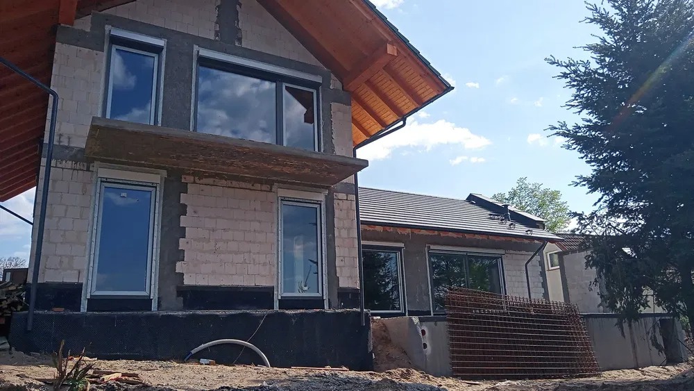 Dom w stanie surowym w Opalenicy z zamontowanymi oknami z roletami zewnętrznymi, widoczne przygotowania do dalszych prac wykończeniowych.