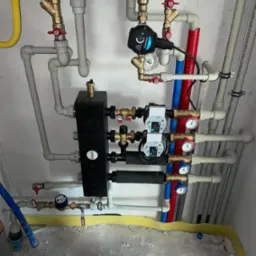 Kompleksowa instalacja hydrauliczna z piecem gazowym Immergas, widoczne pompy obiegowe Wilo, czarny rozdzielacz Womix, rury PEX w kolorach szarym, czerwonym i niebieskim, manometry z czerwonymi...