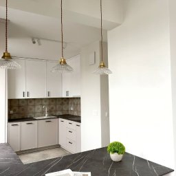Volodymyr Dubov INVO-Bud - Nowoczesna, jasna kuchnia w Warszawie z białymi szafkami, czarnym blatem z marmurowym wzorem, mozaiką nad blatem roboczym i trzema wiszącymi lampami z kloszami z żłobionego szkła.