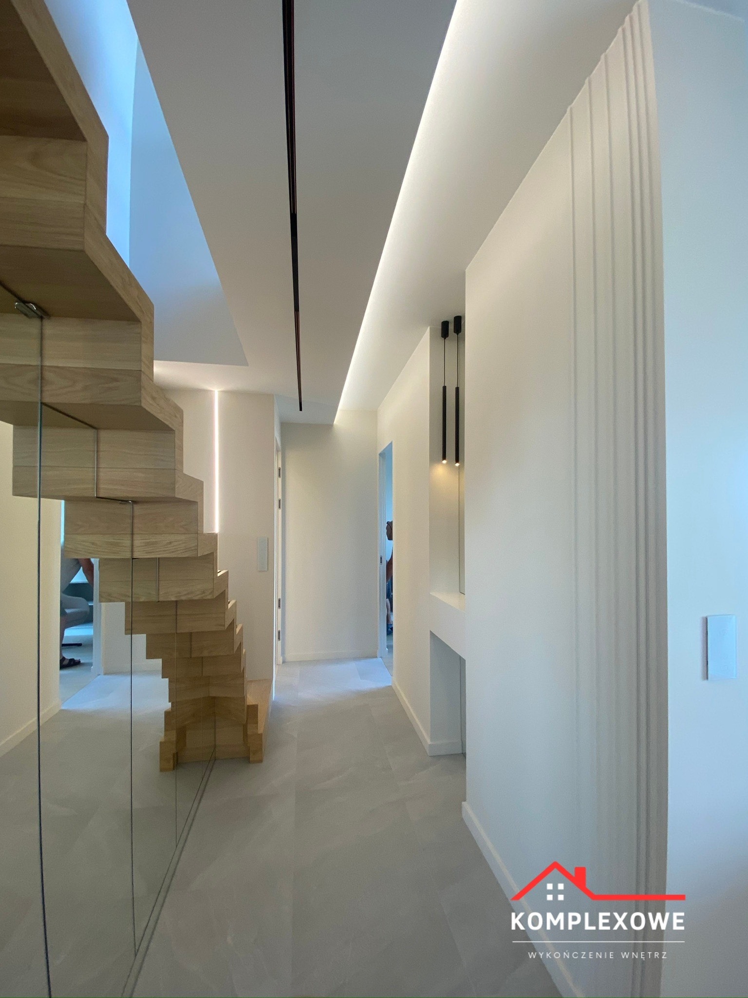 Nowoczesny korytarz z drewnianymi schodami z elementami szkła, oświetleniem LED w suficie i na ścianach, oraz szarą podłogą. Ściany pomalowane na biało z dekoracyjnymi pionowymi żłobieniami. W tle...