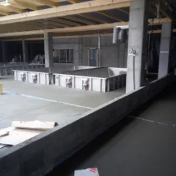 Wnętrze w stanie surowym w Rogoźniku z podłogą wylewaną maszynowo, widoczne betonowe słupy, drewniana konstrukcja dachu i przygotowane zbiorniki.