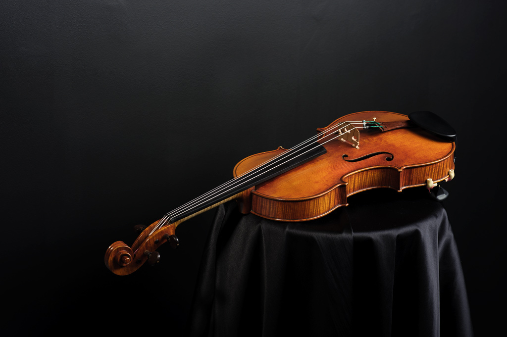 Wysokiej jakości, brązowy skrzypce leżące na czarnej, satynowej tkaninie, z ciemnym tłem.