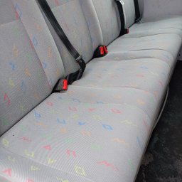 SLY master - Szara tapicerka samochodowa z kolorowym wzorem geometrycznym, widoczne pasy bezpieczeństwa z czerwonymi elementami.