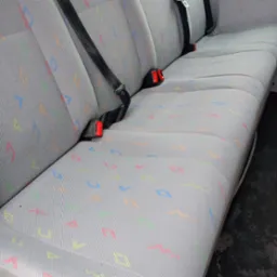 Szara tapicerka samochodowa z kolorowym wzorem geometrycznym, widoczne pasy bezpieczeństwa z czerwonymi elementami.