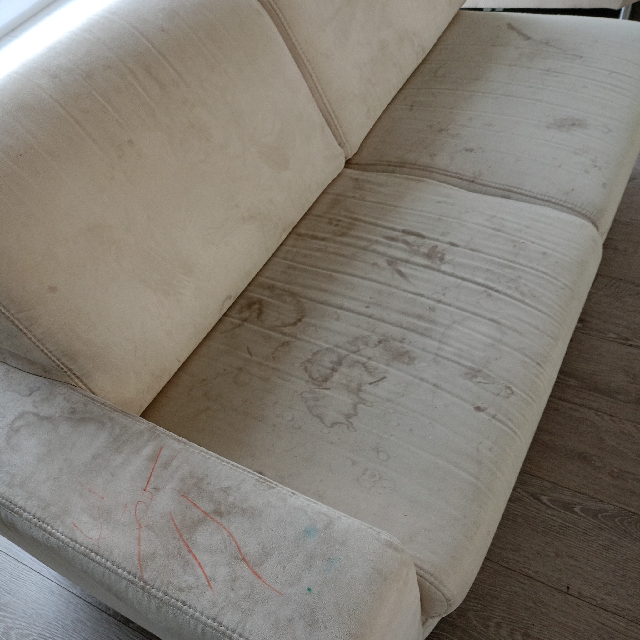 Beżowa kanapa z widocznymi plamami i zabrudzeniami na siedzisku oraz rysunkami wykonanymi kredkami na boku.