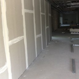 Solid-Art - Montaż płyt gipsowo-kartonowych na ścianie w przestrzeni komercyjnej, widoczne szpachlowane łączenia i instalacja wentylacyjna pod sufitem.