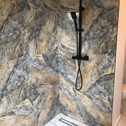 Solid-Art - Kabina prysznicowa z czarną armaturą i płytkami imitującymi marmur w odcieniach szarości, beżu i brązu, widoczny odpływ liniowy w podłodze wyłożonej białymi płytkami z szarymi żyłkami.