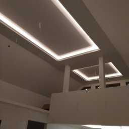 Solid-Art - Nowoczesny sufit podwieszany z oświetleniem LED w dwupoziomowym wnętrzu, widok z dołu na rusztowanie.