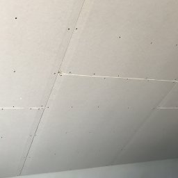 Solid-Art - Płyty gipsowo-kartonowe zamontowane na skośnym poddaszu, widoczne ślady po wkrętach, łączenia płyt wypełnione masą szpachlową, fragment ocieplenia widoczny w rogu.