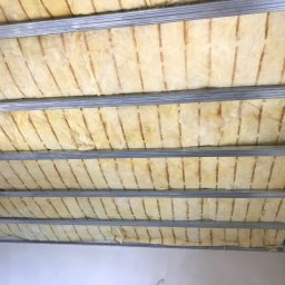 Solid-Art - Poddasze w trakcie ocieplania: wełna mineralna umieszczona między metalowymi profilami konstrukcji sufitu podwieszanego, widoczne niedociągnięcia w ułożeniu izolacji.