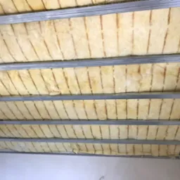 Poddasze w trakcie ocieplania: wełna mineralna umieszczona między metalowymi profilami konstrukcji sufitu podwieszanego, widoczne niedociągnięcia w ułożeniu izolacji.