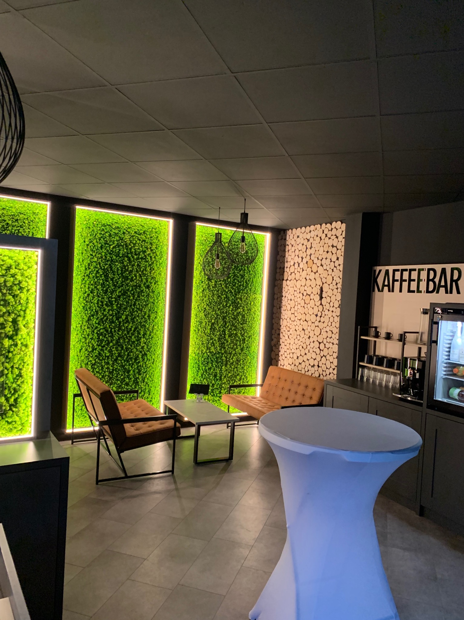 Nowoczesna aranżacja wnętrza kawiarni z panelami z mchu, ścianą z drewnianych krążków, designerskimi lampami i meblami w stylu retro.